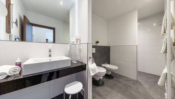 Ein modernes Badezimmer mit einem großen Spiegel, einem weißen Waschbecken und zwei Toiletten.