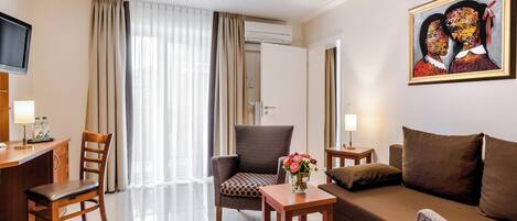 Habitación de hotel con sofá, dos sillas, una mesita con un jarrón de flores, televisión y un cuadro en la pared.