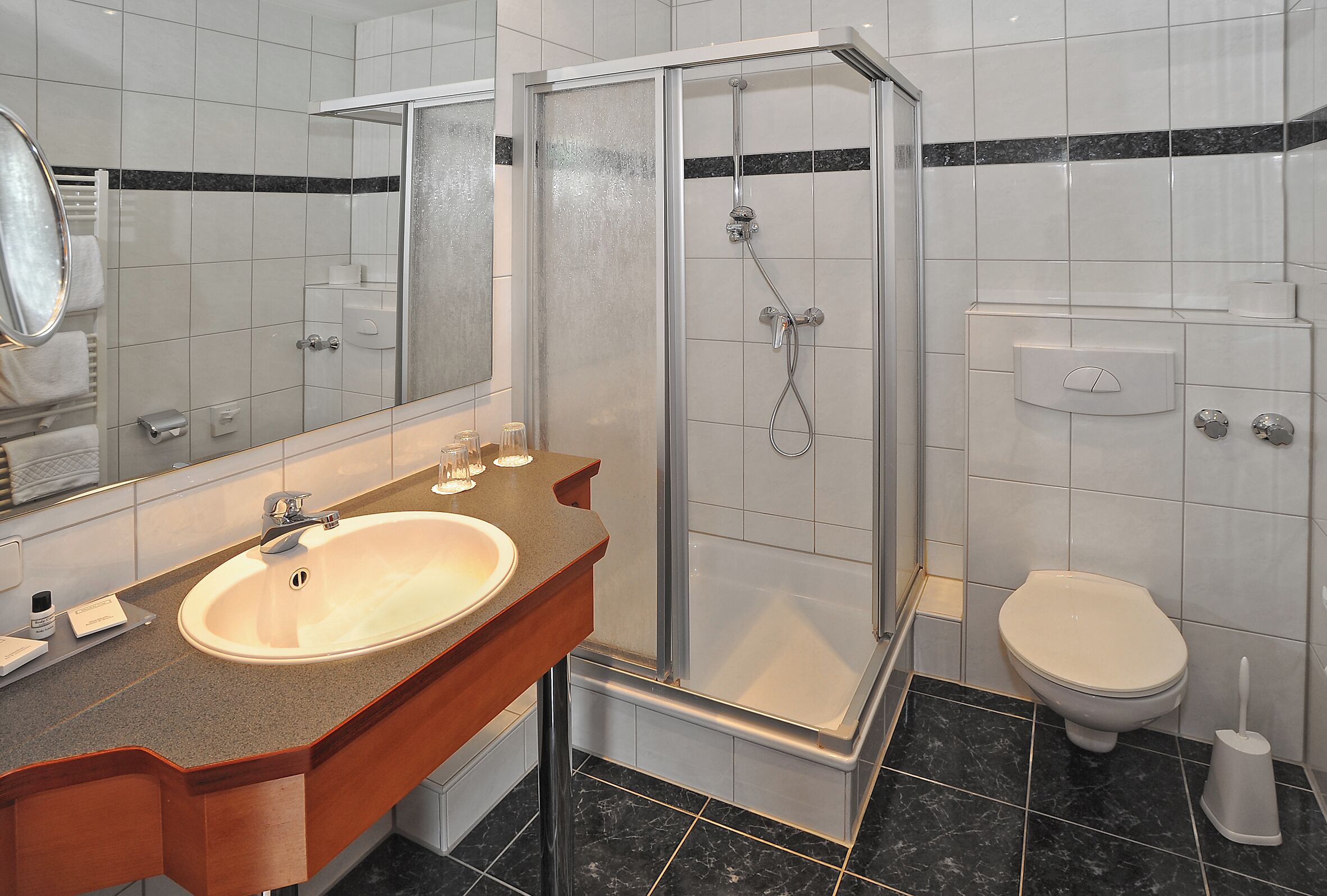 Un baño con lavamanos, espejo, ducha, inodoro y un perchero para toallas.
