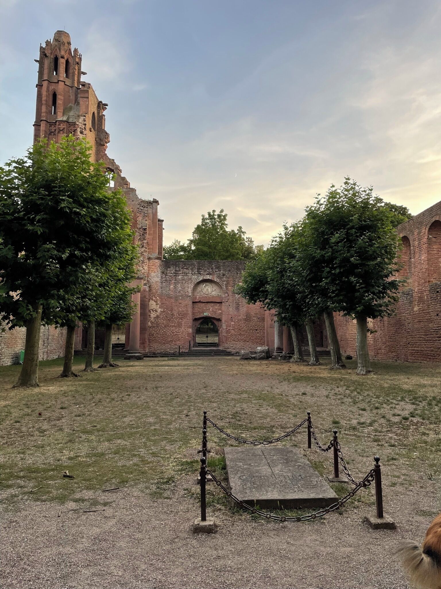 Un ancien bâtiment en briques, doté d’une haute tour, entouré d’arbres et d’une zone délimitée par une clôture.