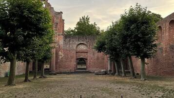 An ancient brick building with a tall tower, surrounded by trees and a fenced area.
