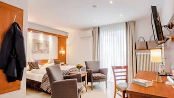 Ein Hotelzimmer mit Bett, zwei Sesseln, einem Schreibtisch, einem Fernseher und einem fensterbepflanzten Fenster.