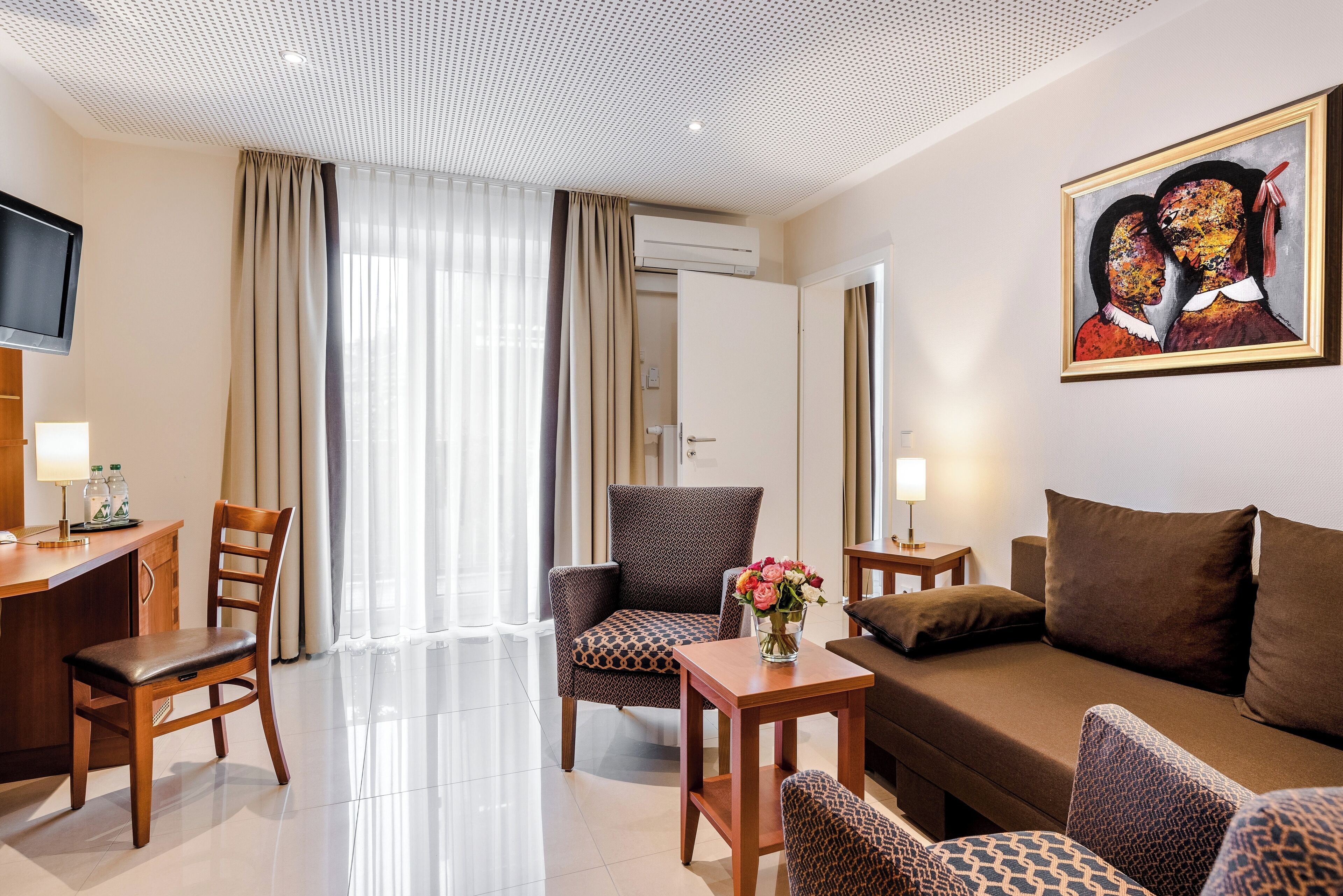 A hotel room with a sofa, chairs, a desk, a TV, and a painting.
