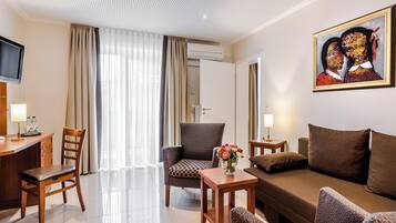 A hotel room with a sofa, chairs, a desk, a TV, and a painting.