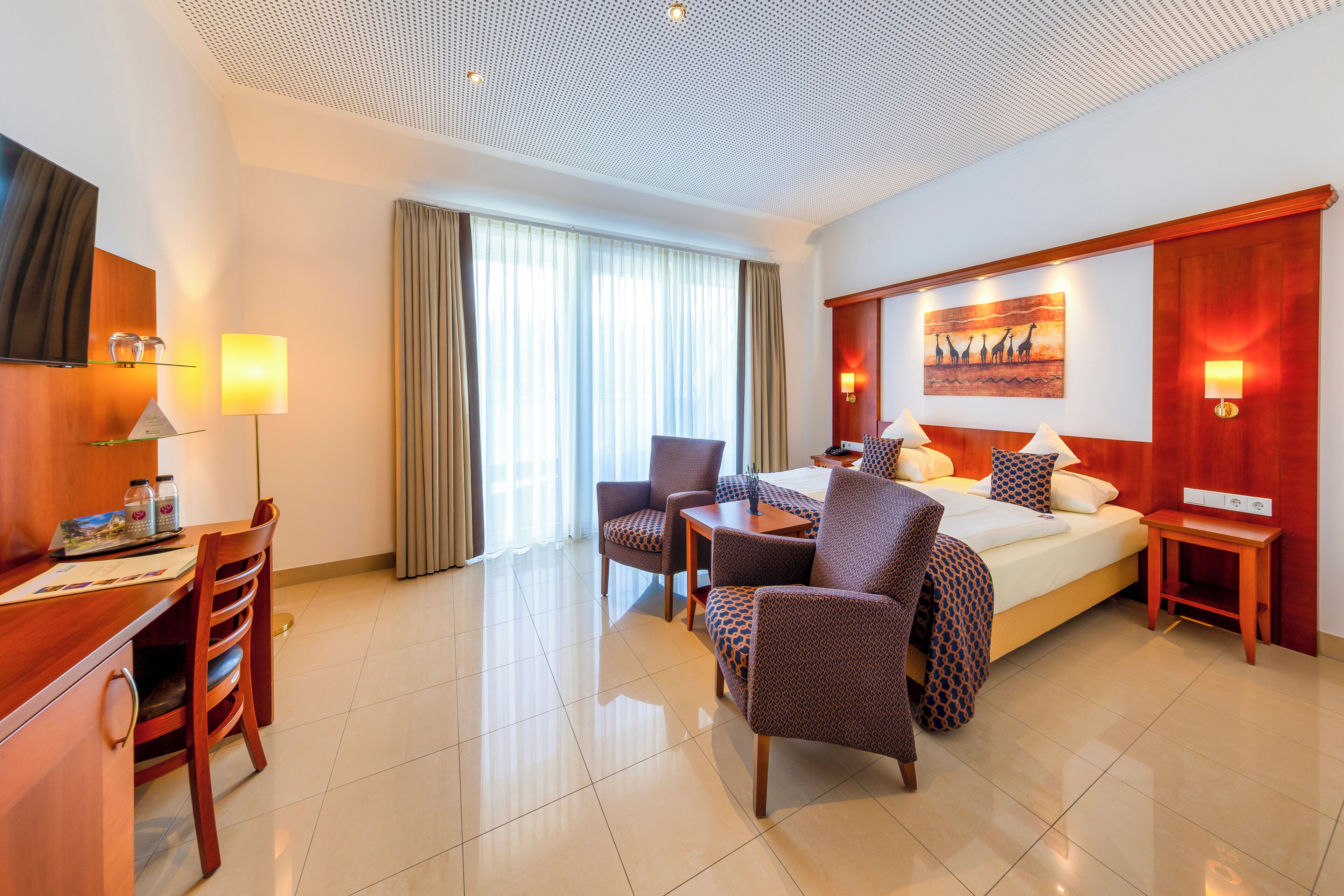 Habitación de hotel con cama, dos sillones, un escritorio, un televisor y un cuadro en la pared.