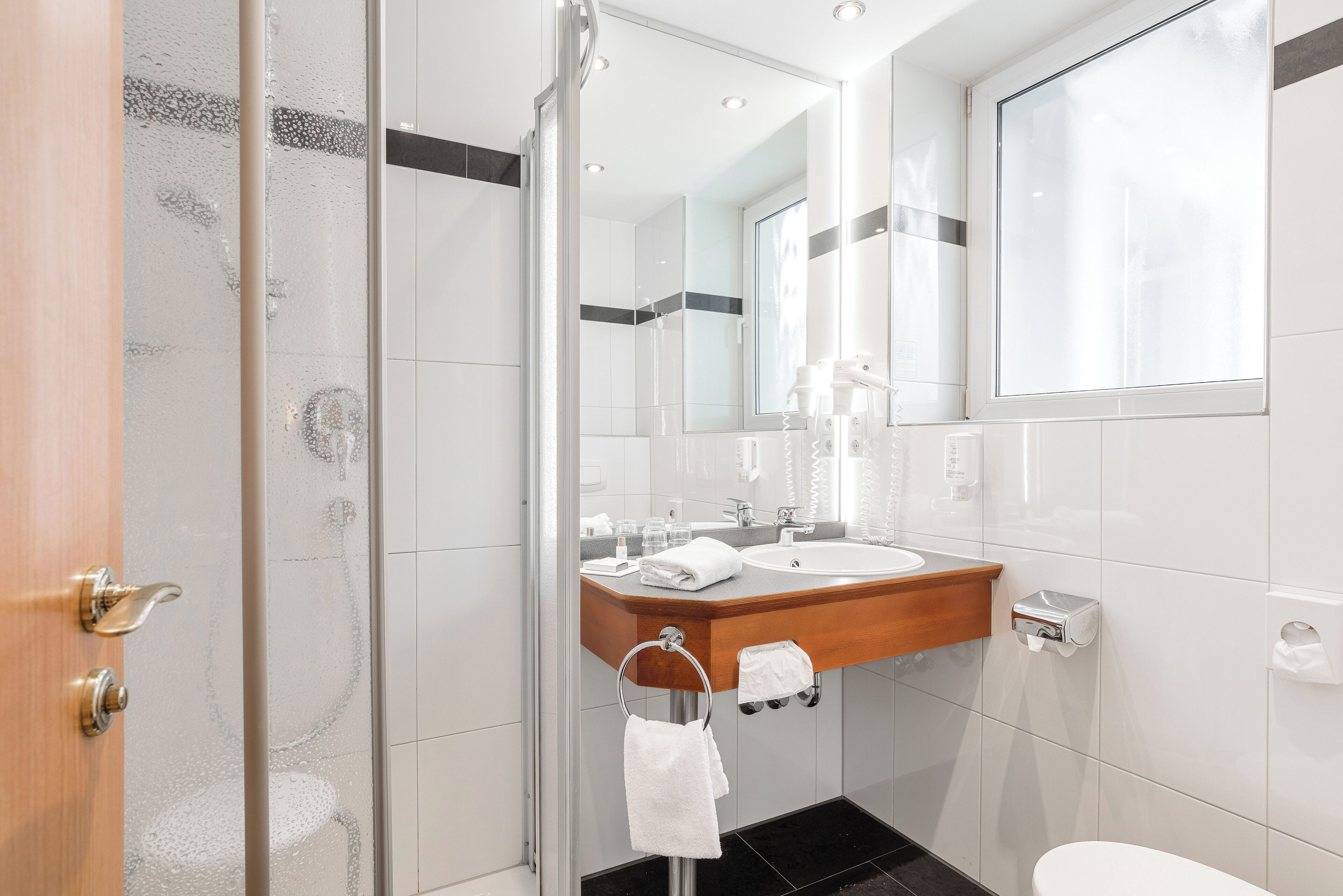 Un baño moderno con cabina de ducha de vidrio, tocador de madera, un espejo grande y un inodoro.