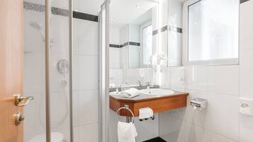 Un baño moderno con cabina de ducha de vidrio, tocador de madera, un espejo grande y un inodoro.