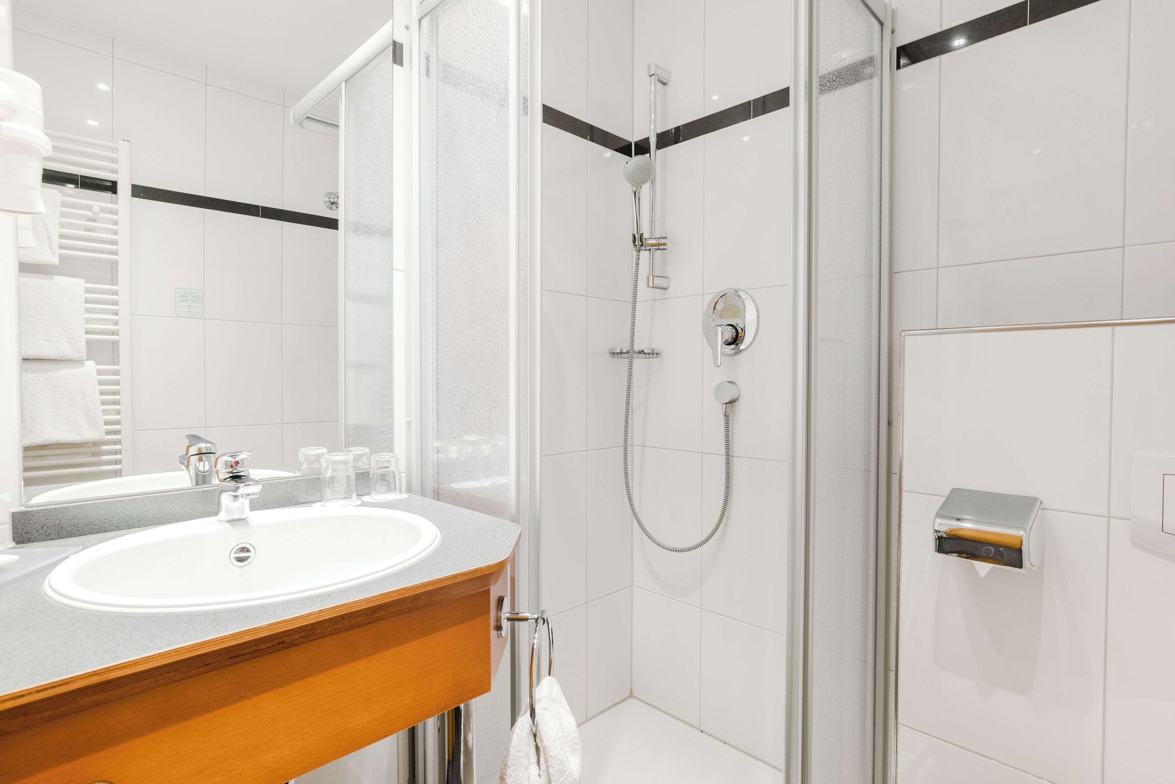A modern bathroom with a white sink, a mirror, and a glass-enclosed shower.