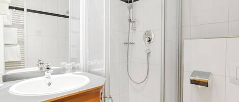 A modern bathroom with a white sink, a mirror, and a glass-enclosed shower.