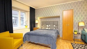 A bedroom with a bed, a yellow armchair, a wardrobe, and a window with curtains. - Town Hall Square Apartments - 1 Bdr (Tallinn)