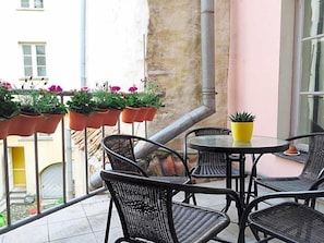 A balcony with wicker chairs and a round table, potted plants, and a view of a building.