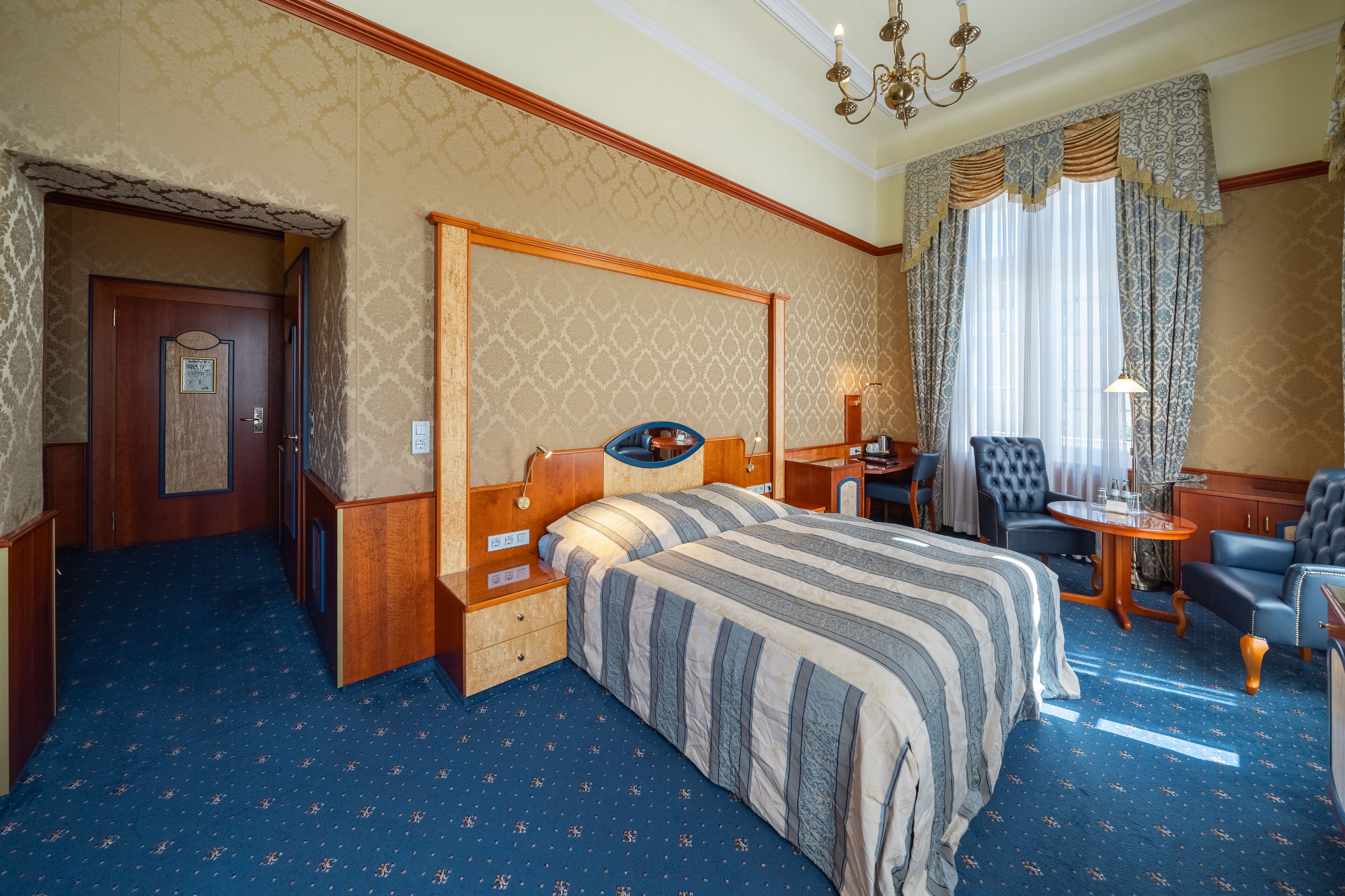 A hotel room with a large bed, a desk, a chair, and a small table.