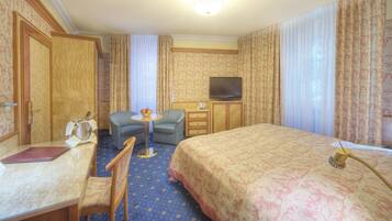 Ein Hotelzimmer mit Bett, Schreibtisch mit Stuhl, einem kleinen Tisch mit Lampe, Fernseher und Vorhängen.