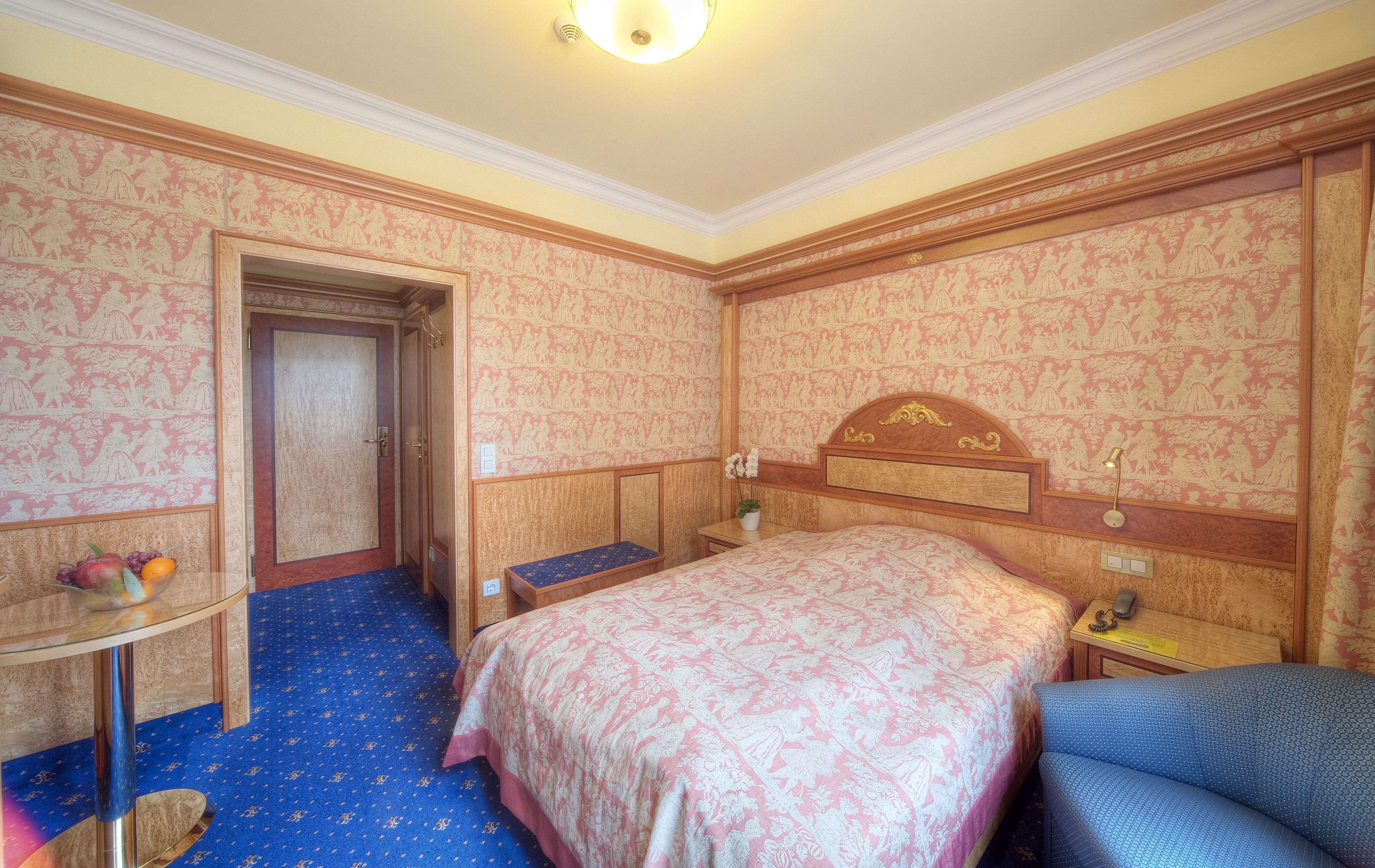 A hotel room with a bed, a desk, a chair, and a small table with fruit.