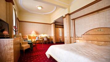 A hotel room with a large bed, a desk with a chair, a sofa, and a small table with a lamp.