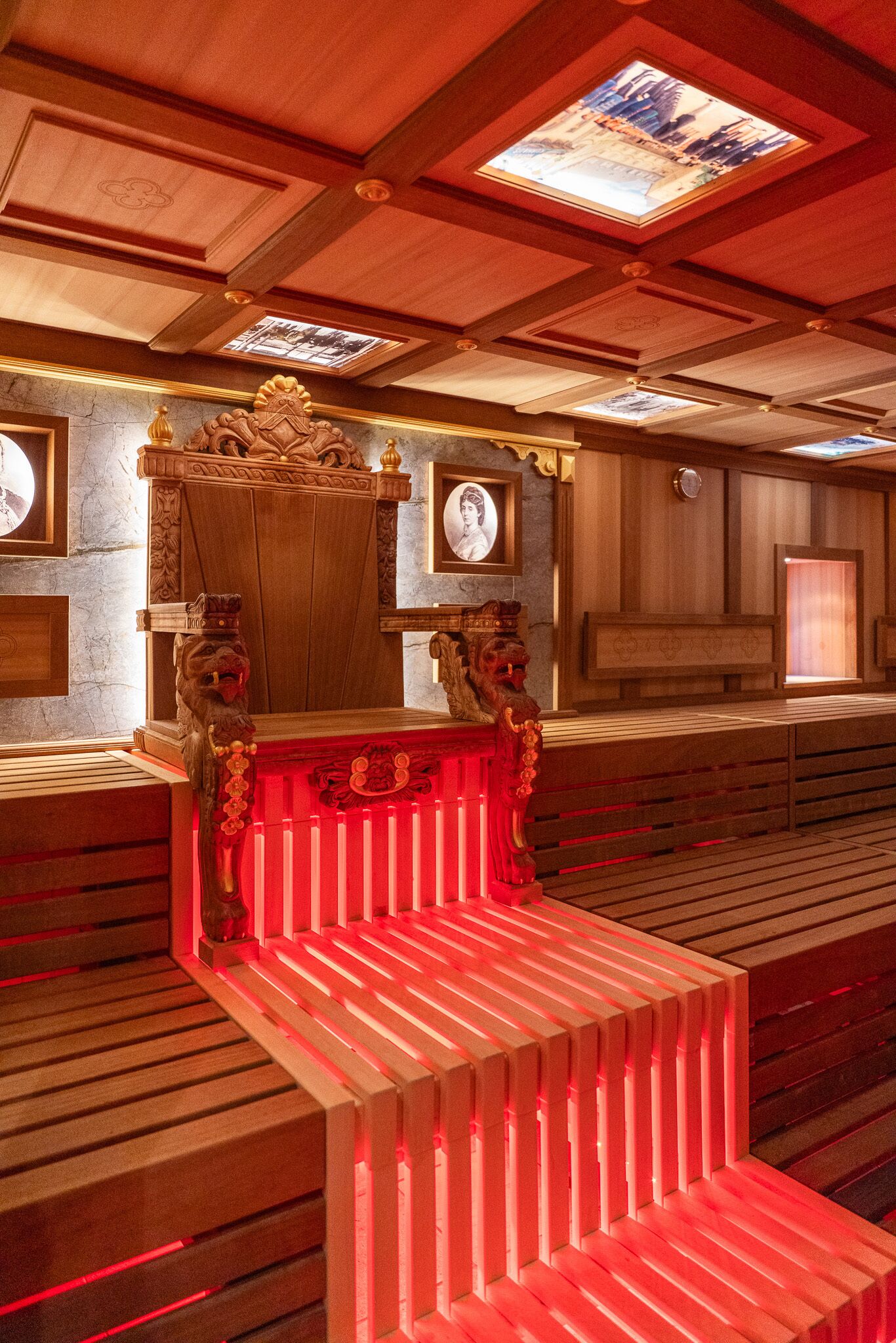 Un área con bancos de madera, una estructura iluminada con luz roja, paneles de madera y un tragaluz.