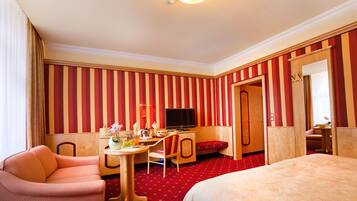 Ein Hotelzimmer mit gestreifter Tapete, einem Bett, einem Schreibtisch mit Stuhl, einem Fernseher und einem kleinen Tisch mit Blumen in einer Vase.