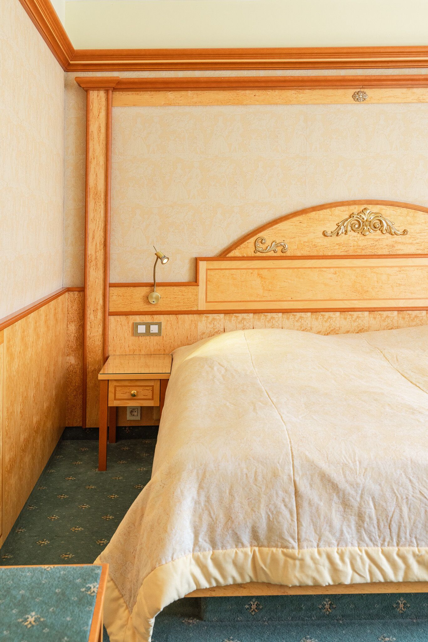 A hotel room with a wooden headboard, a bedside table with a lamp, and a bed with a beige bedspread.