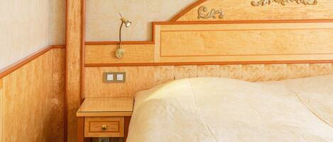 A hotel room with a wooden headboard, a bedside table with a lamp, and a bed with a beige bedspread.