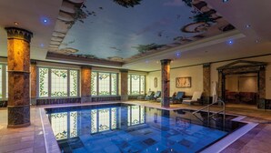 A large indoor swimming pool with a clear blue water surface, surrounded by stone columns and decorative ceiling artwork. - Häcker's Grand Hotel Bad Ems (Bad Ems)