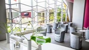 Un interior moderno con una zona de estar que incluye sofás y sillones grises, un mostrador de recepción blanco y un amplio ventanal con un diseño geométrico.