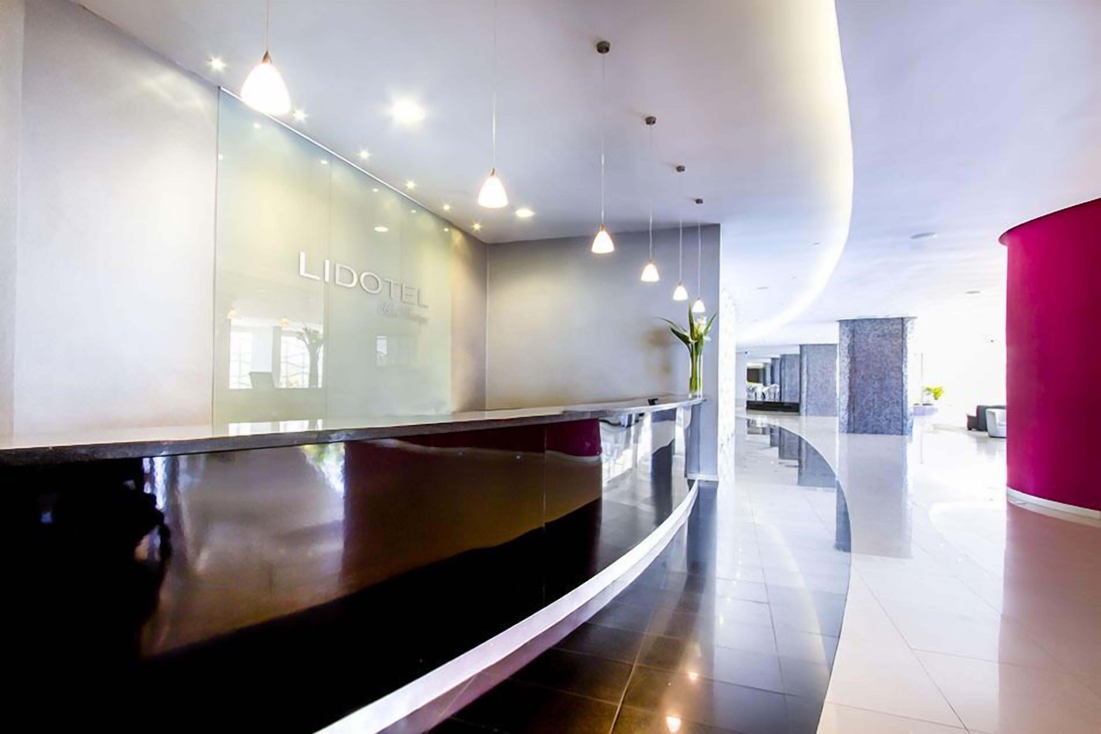 A modern hotel reception area with a curved reception desk, glass walls, and pendant lighting.