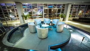 Un área interior de piscina moderna con asientos y vistas del paisaje urbano a través de amplios ventanales.