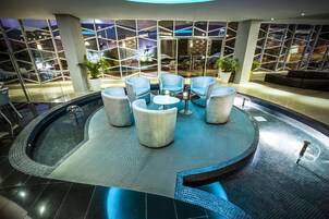 Un área interior de piscina moderna con asientos y vistas del paisaje urbano a través de amplios ventanales.