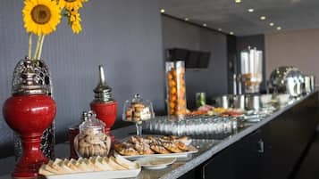 Montaje de bufé con diversas opciones de comida, incluyendo pasteles y un frasco de galletas, en un ambiente moderno de hotel.