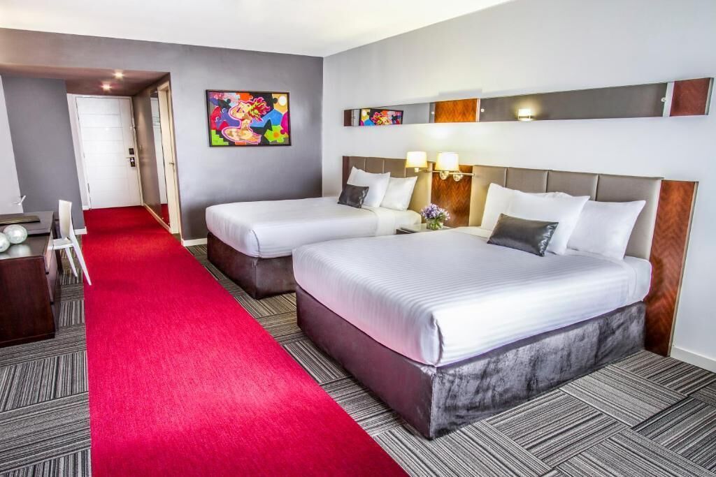 Una habitación de hotel con dos camas, una alfombra roja y un cuadro en la pared.