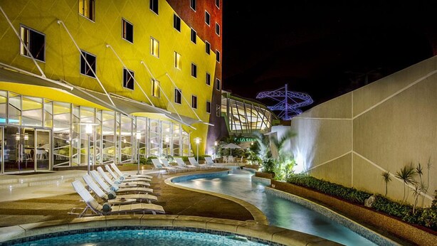 Un hotel con zona de piscina, sillones de descanso y un edificio de fachada amarilla.