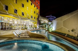 Un hotel con zona de piscina, sillones de descanso y un edificio de fachada amarilla.