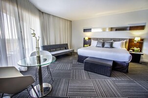 Una habitación de hotel moderna con una cama grande, una mesa de vidrio, un sofá y un banco.