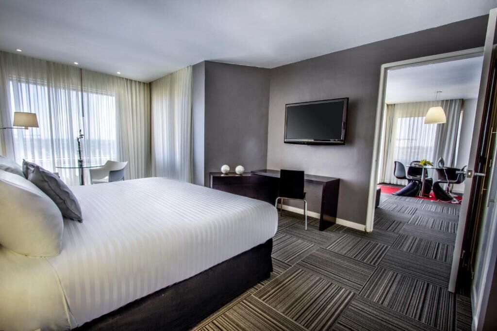 Quarto de hotel moderno com uma cama grande, uma escrivaninha, uma televisão de tela plana e um espelho.