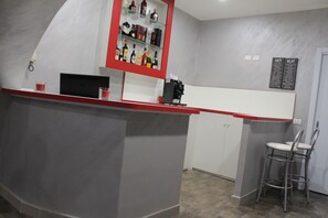 A bar area with a red counter, shelves with bottles, a coffee menu, and two bar stools. - Residenza Nicola Amore (Naples)