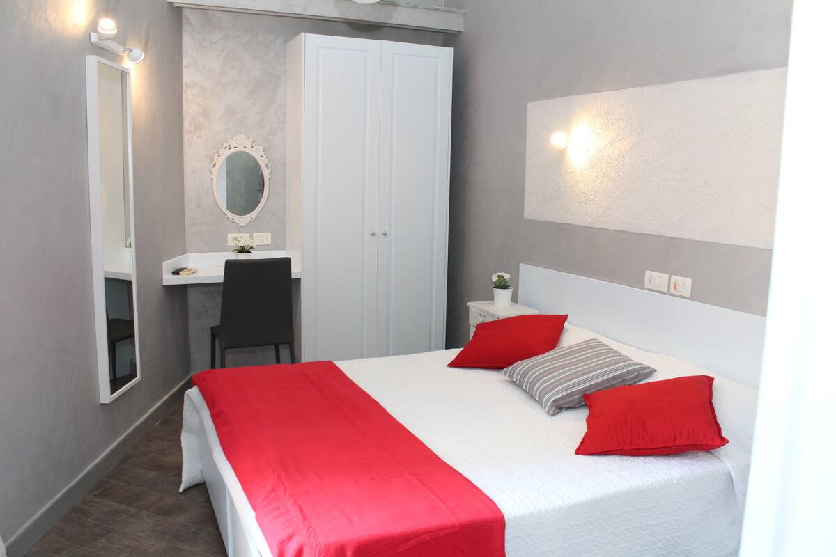 A bedroom with a bed, a desk, a chair, a wardrobe, and a mirror.