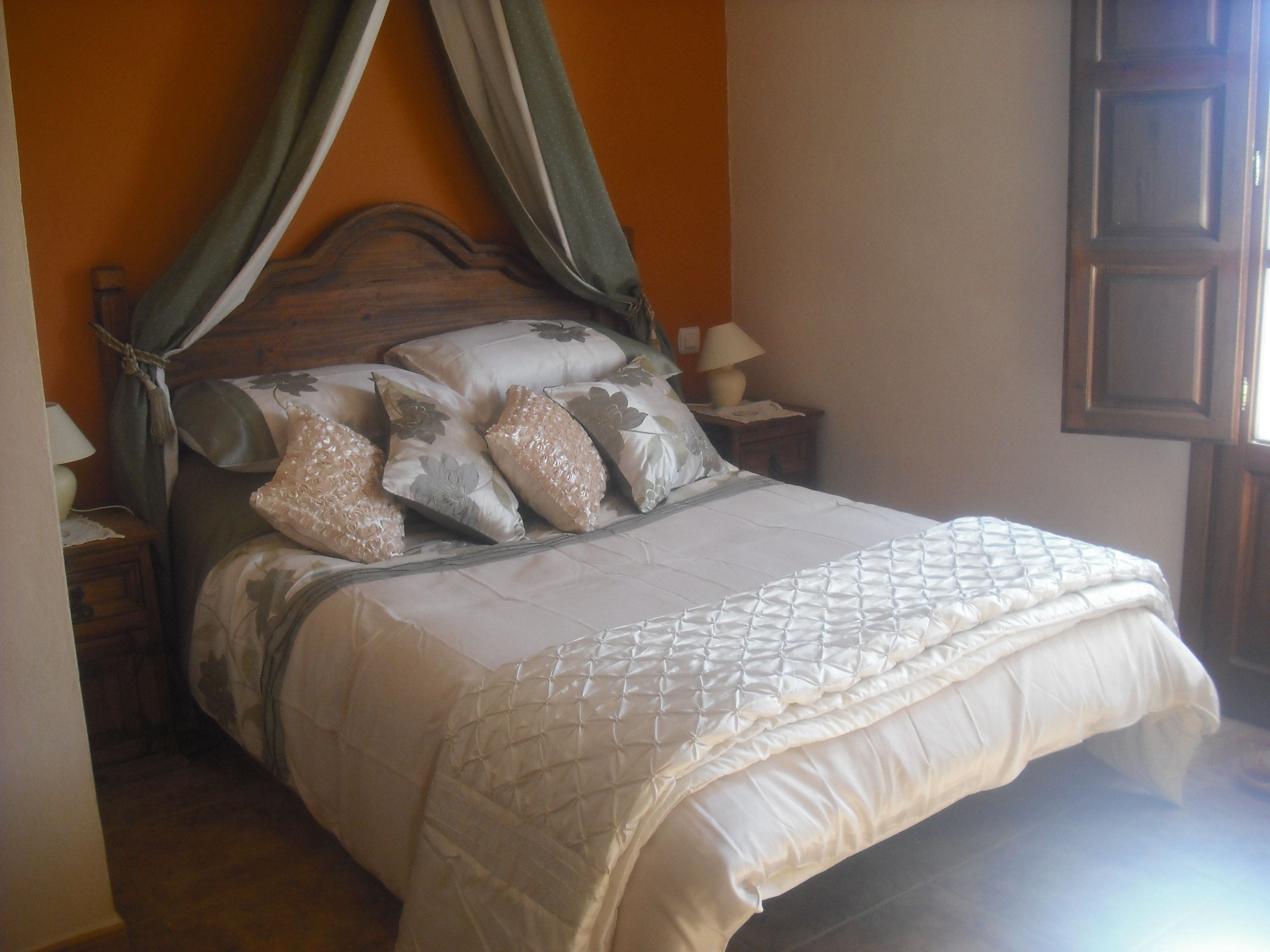 A bed with a canopy, multiple pillows, a bedside table with a lamp, and a window with a view.