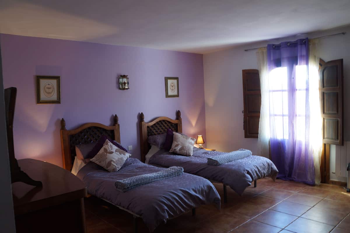 A bedroom with two beds, a nightstand, a lamp, and a window with curtains.