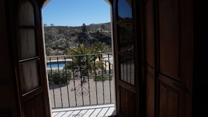 An open wooden door leading to a balcony with a view of a rocky hillside and a pool. - Hotel Los Sibileys (Lorca)