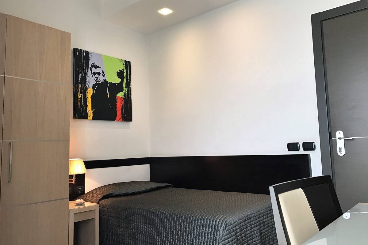 A hotel room with a bed, a nightstand, a lamp, a wardrobe, and a painting on the wall.