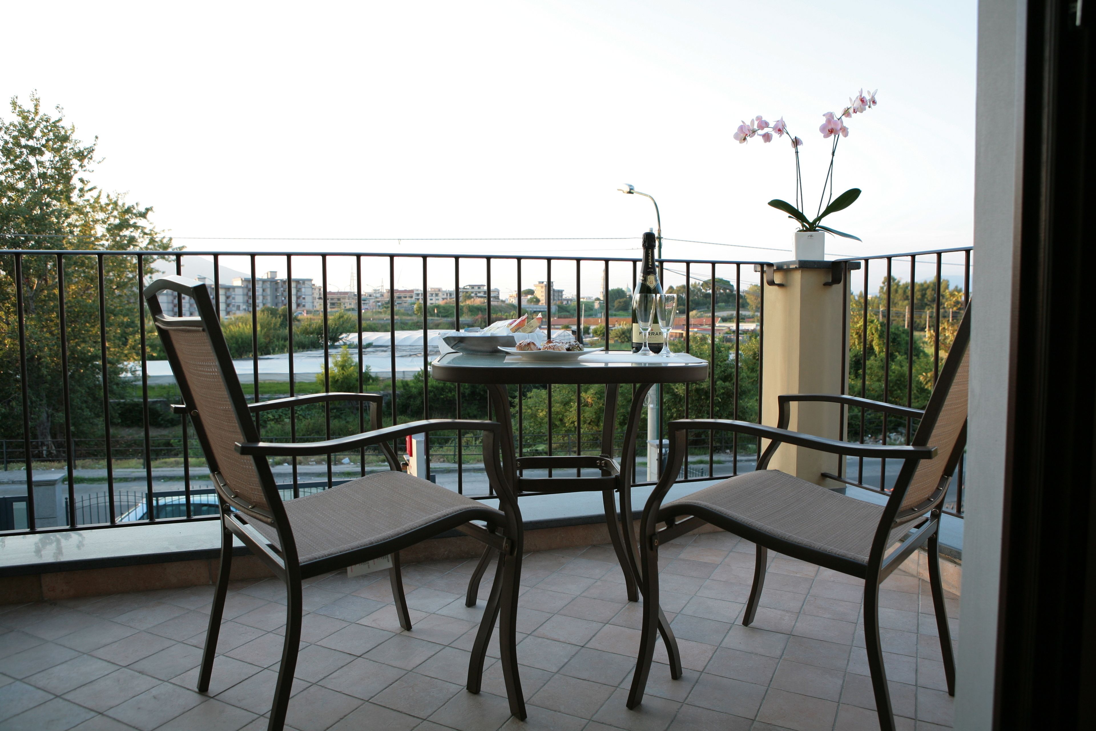 A balcony with two chairs, a table, and a vase with flowers.