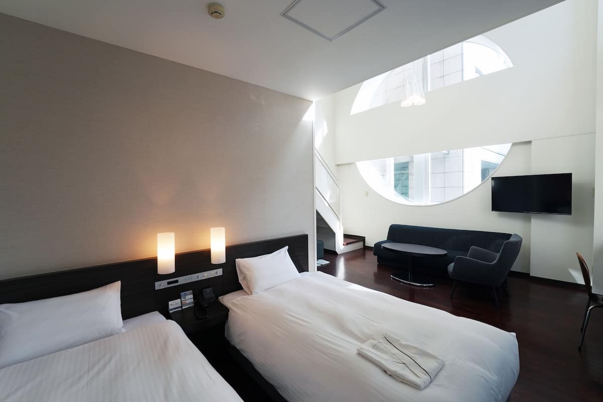 Quarto de hotel com duas camas, um sofá, uma televisão e uma escada que leva a um andar superior.