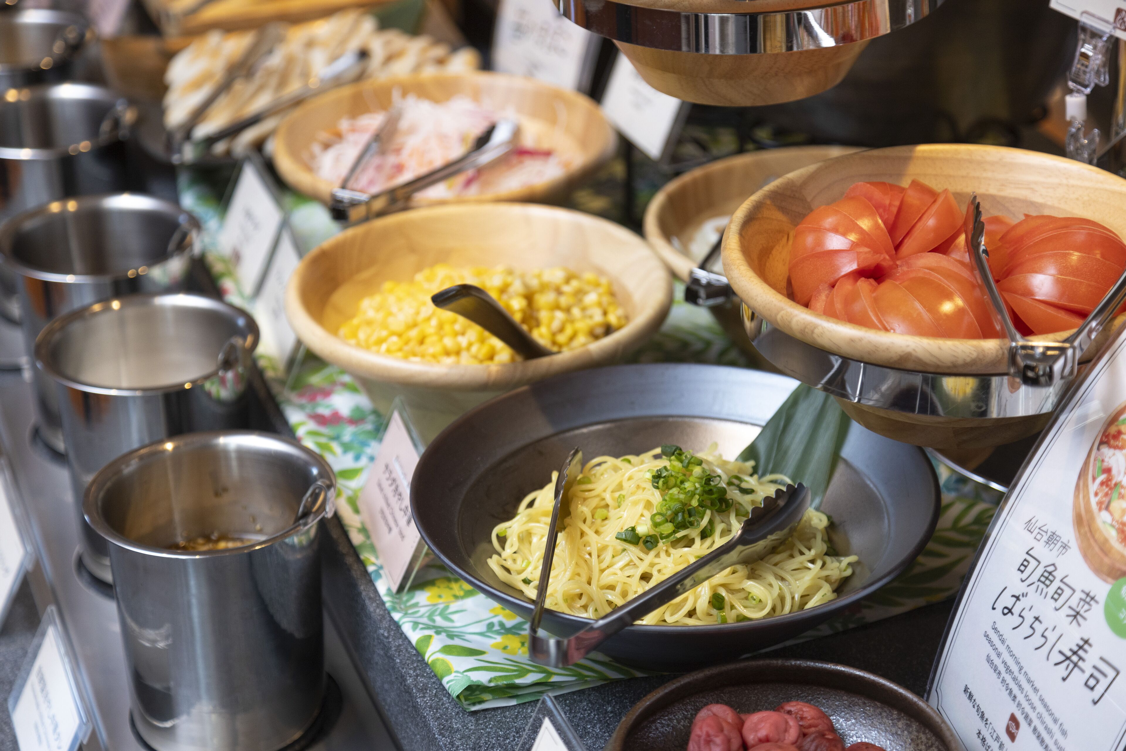 Un bufé con diversos alimentos, como fideos, maíz, tomates y carne.