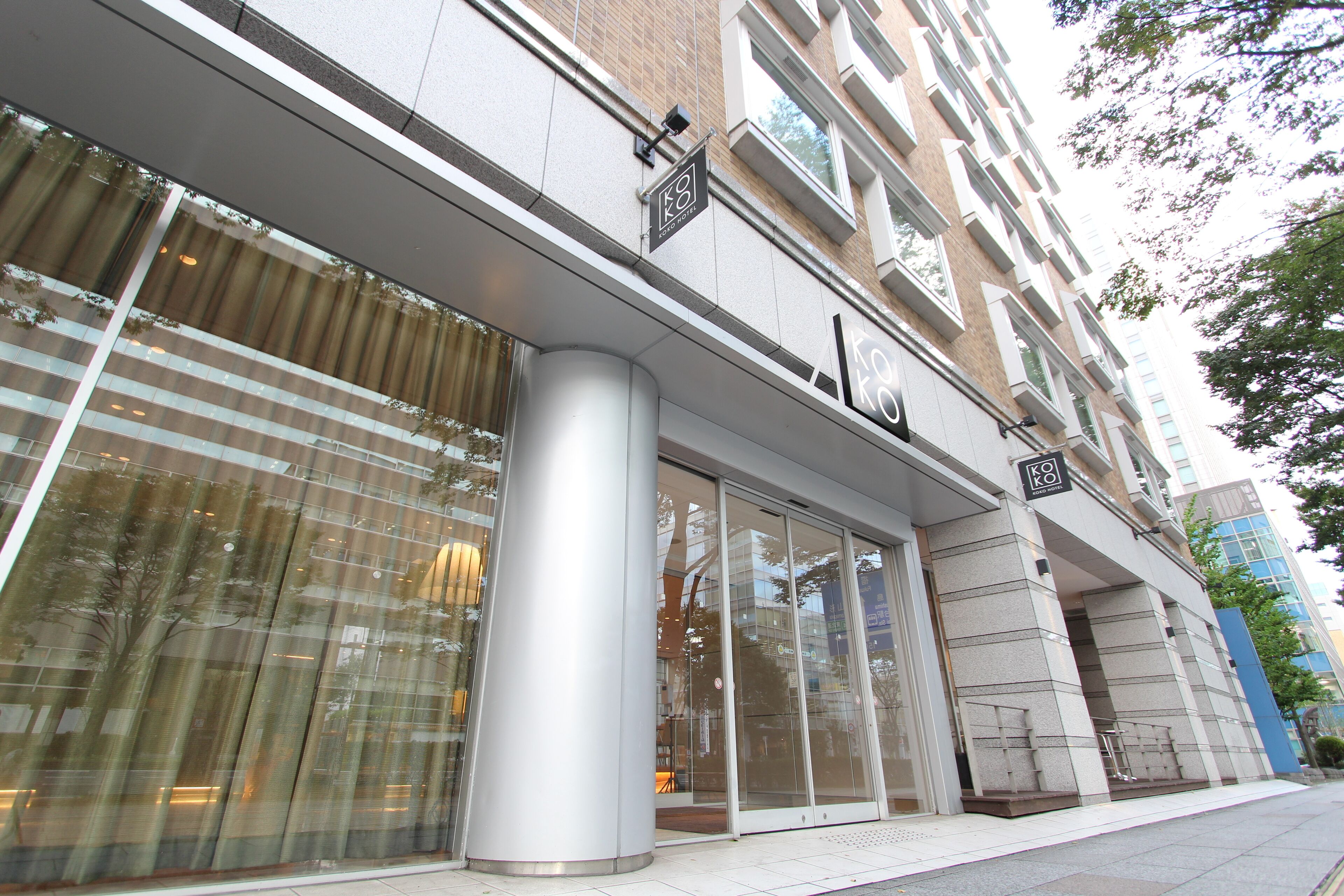 Un edificio moderno con grandes ventanales, una entrada destacada con marquesina metálica, y un letrero que indica espacio de oficinas o negocios.