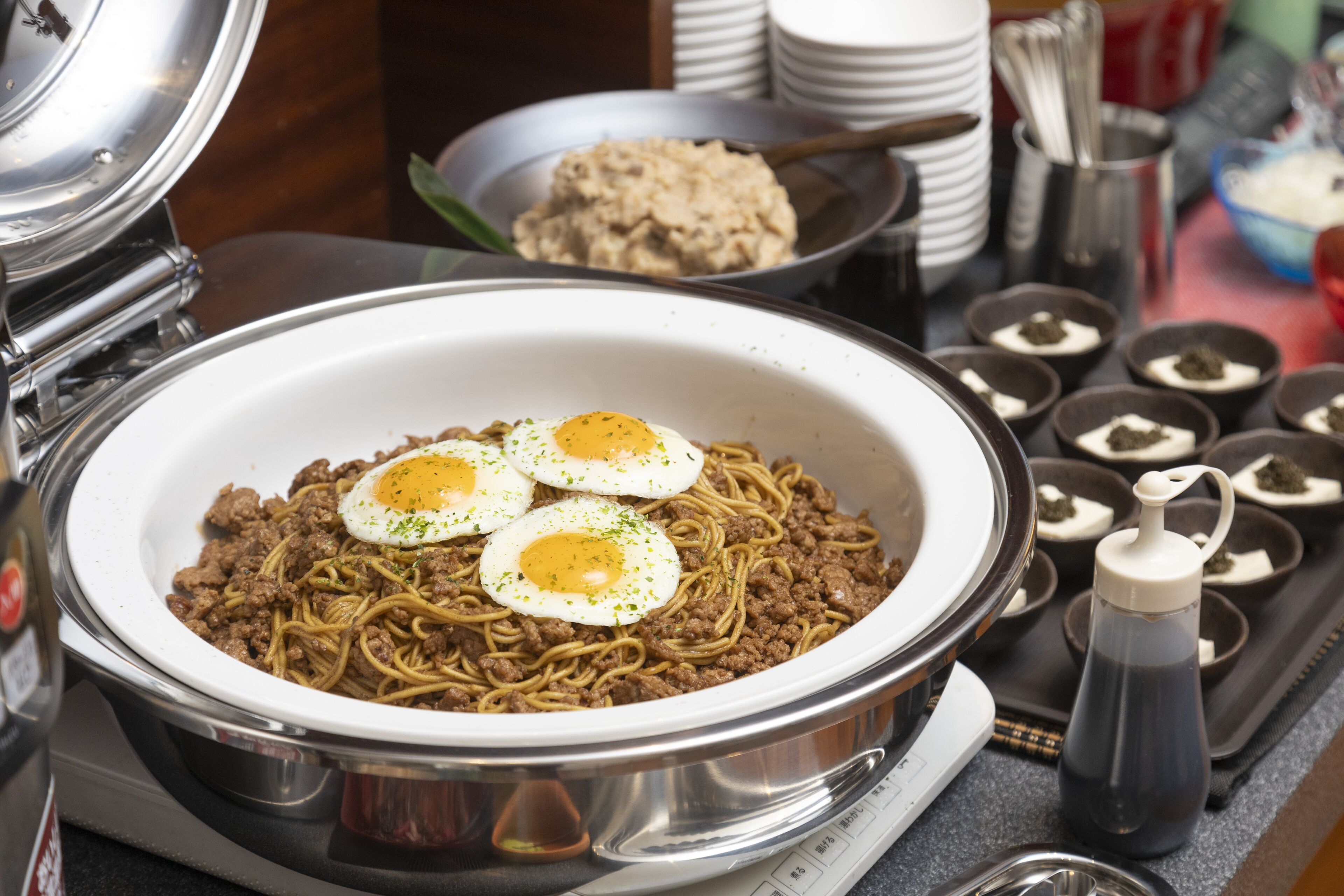 A large bowl of noodles with meat and eggs on a stove.
