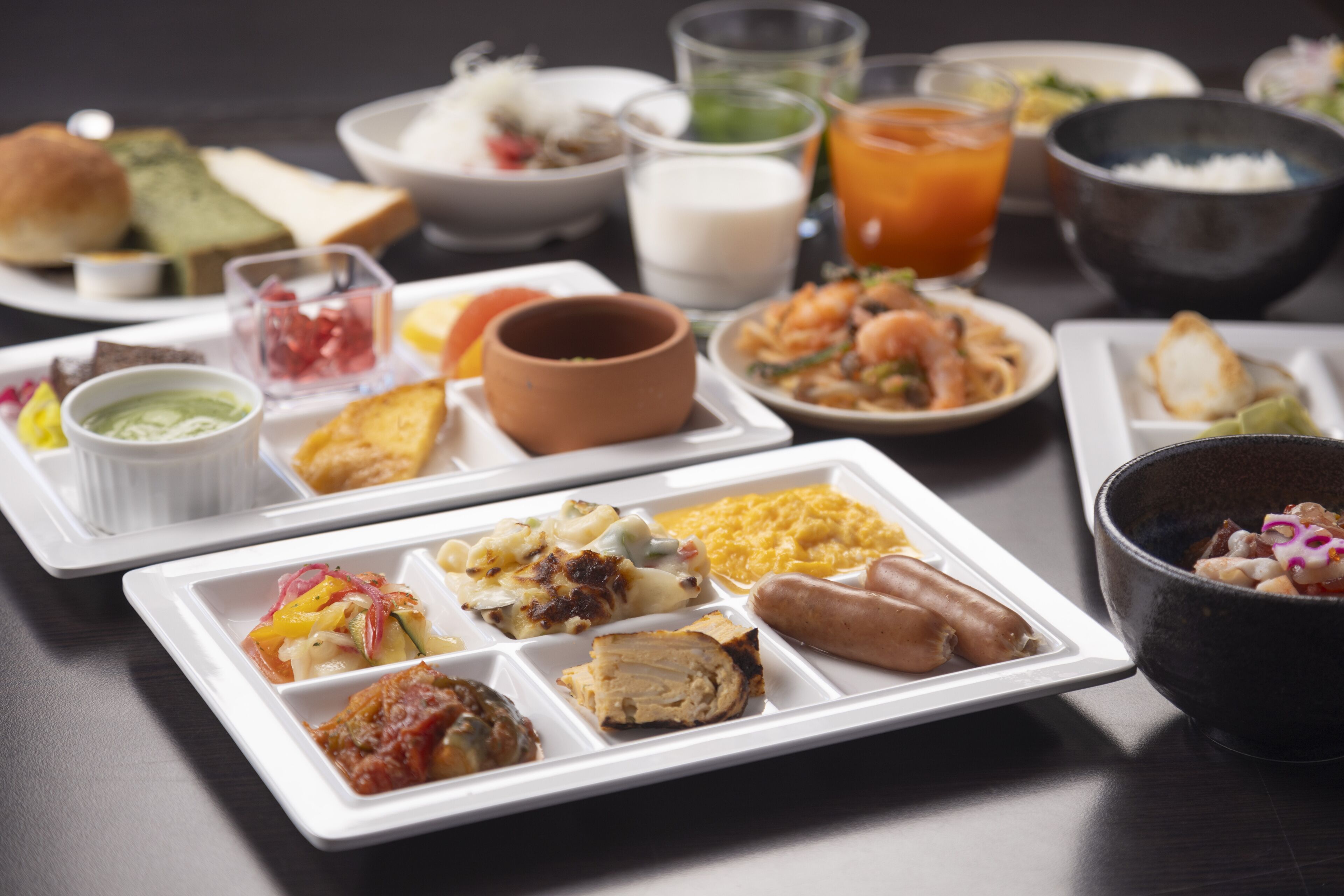 A variety of dishes on a table, including a white plate with multiple food items, a black bowl, and several glasses of beverages.