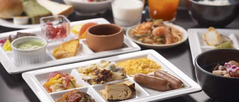 A variety of dishes on a table, including a white plate with multiple food items, a black bowl, and several glasses of beverages.