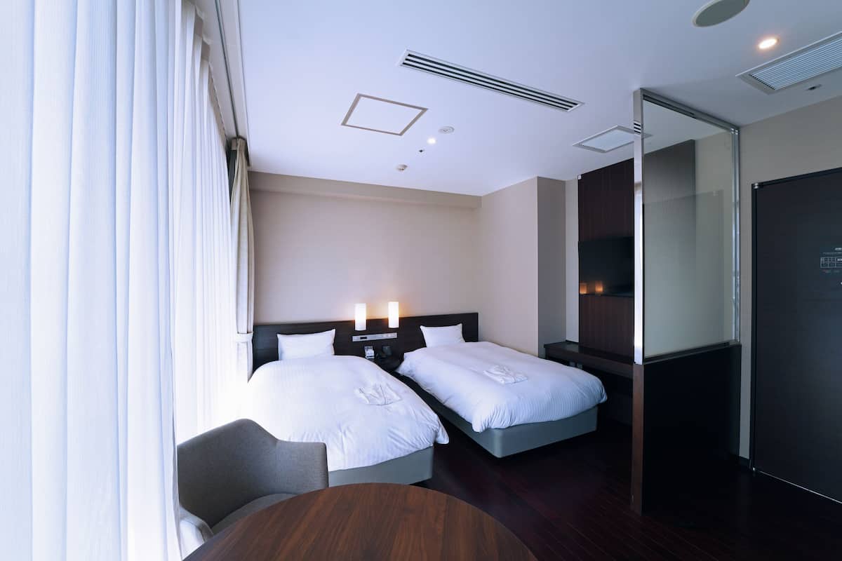Quarto de hotel com duas camas, uma escrivaninha e uma televisão.