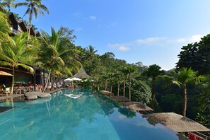 Una piscina con sillas de descanso y sombrillas, rodeada de palmeras y un entorno tropical.