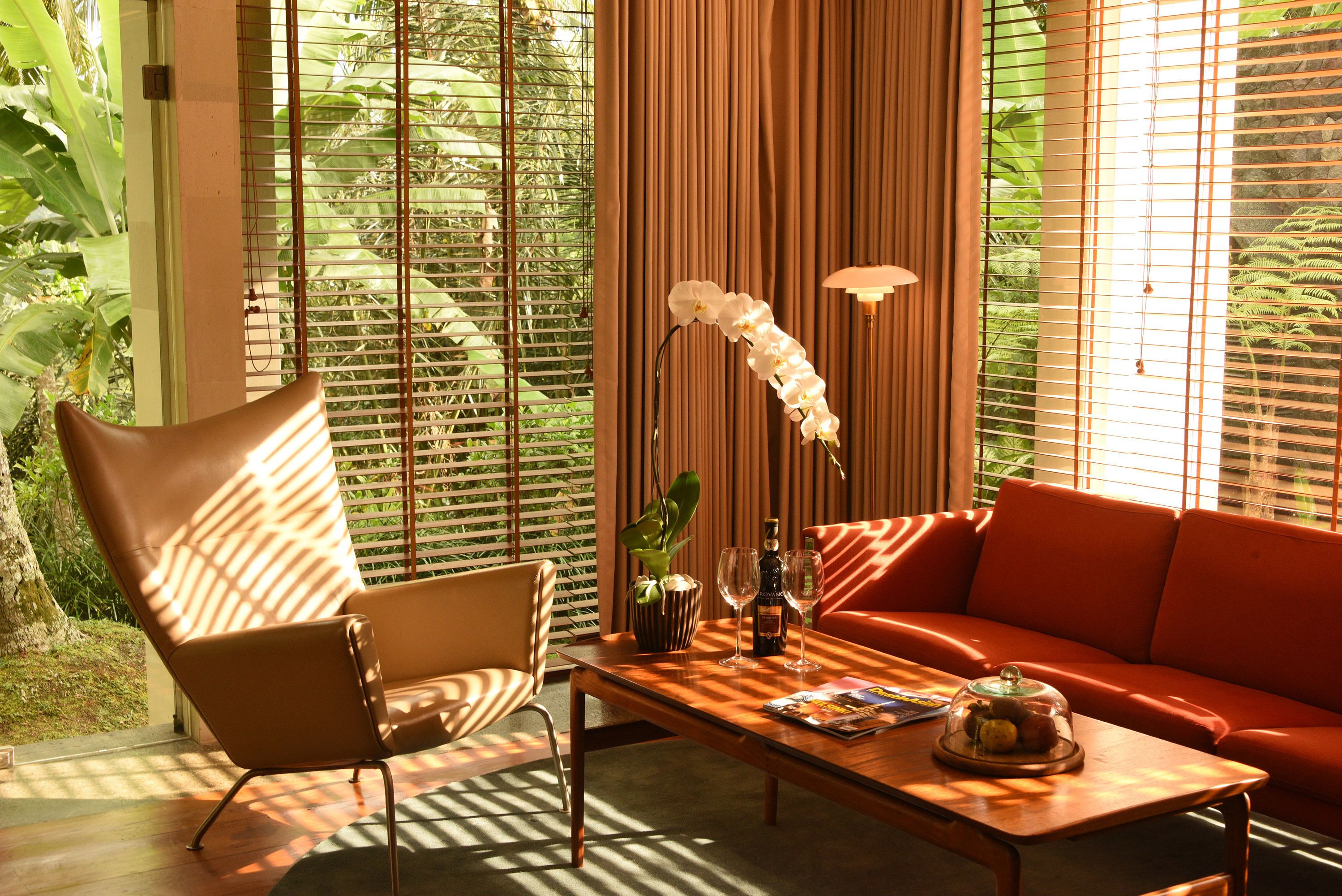 Una sala moderna con un sillón de cuero marrón, un sofá rojo y una mesa de centro de madera con una revista, un vaso y una botella.